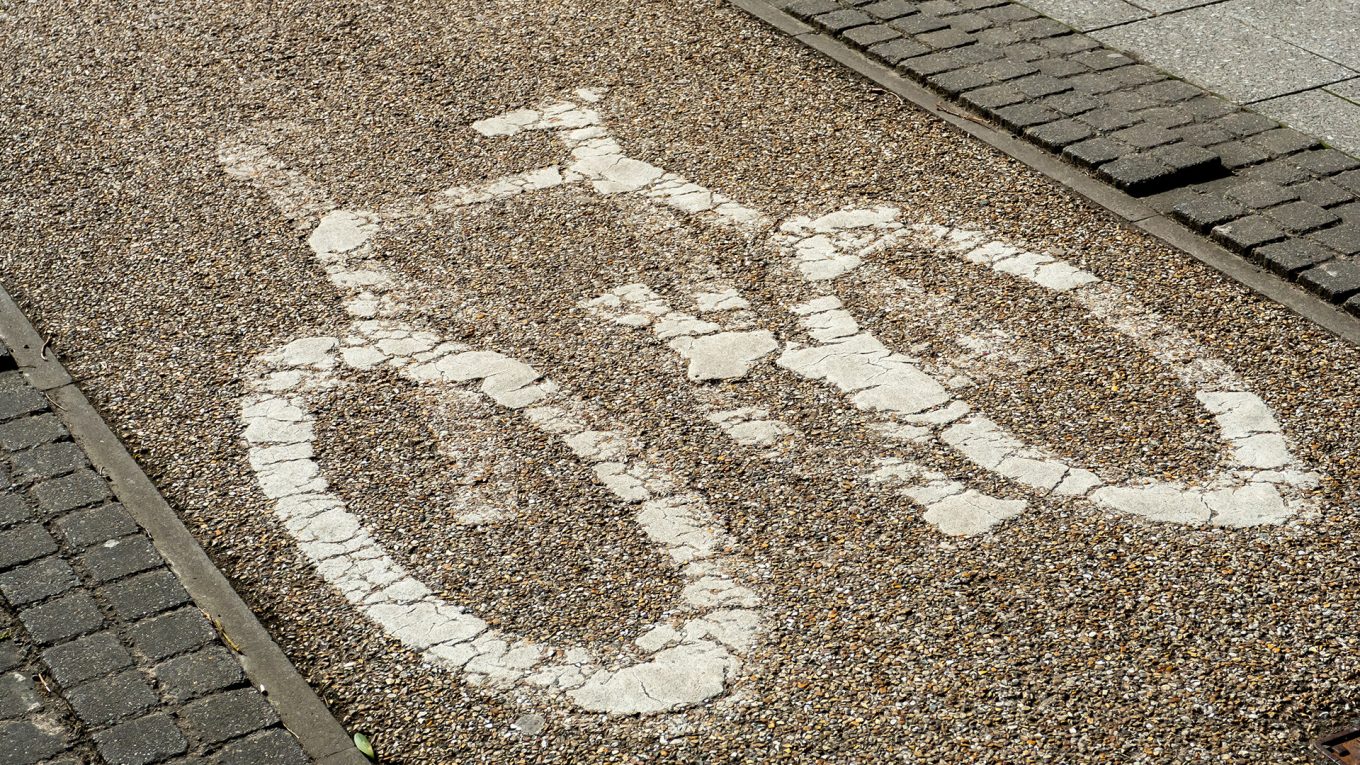 A worn, painted bicycle sign on a narrow cycle lane in Coventry