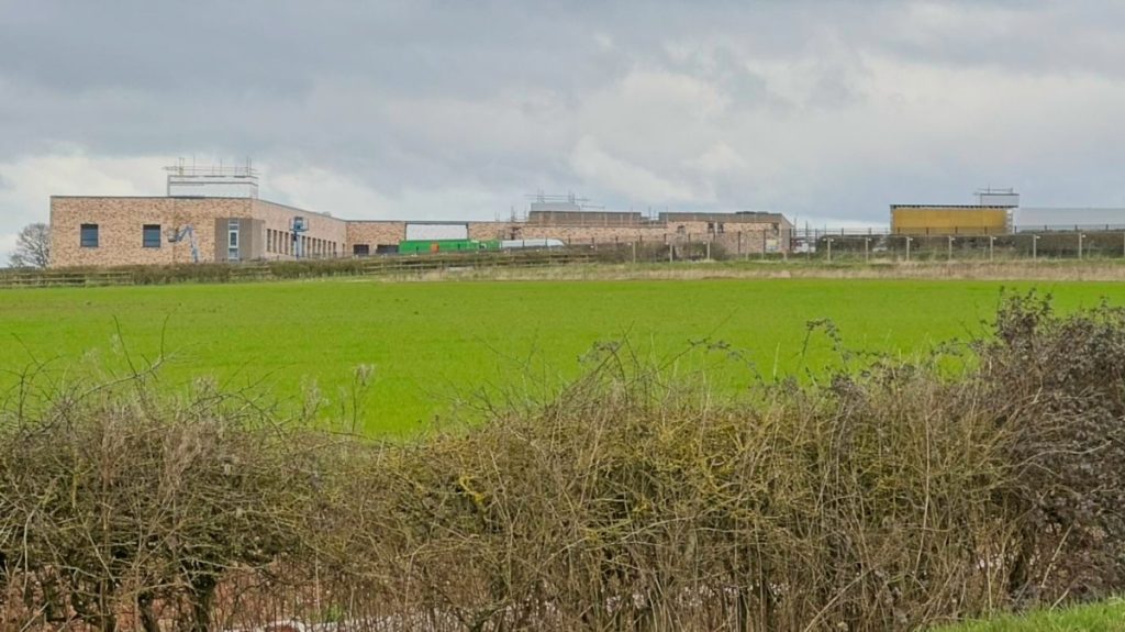 Higham Lane North Academy school under construction, seen in the distance across a green field.