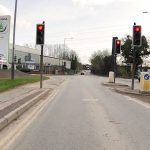 Longford Road southbound, approaching red traffic signals. In the distance, the road runs under a motorway bridge. A Skoda car showroom can be seen to the left.