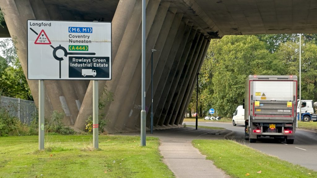Approaching Longford Road/Wilsons Lane/Pickards Way/B4113 Roundabout between Bedworth and Coventry. The road leads away, under the M6. The roundabout sign is visible on the left; a lorry approaches the roundabout in the left lane of the carriageway.
