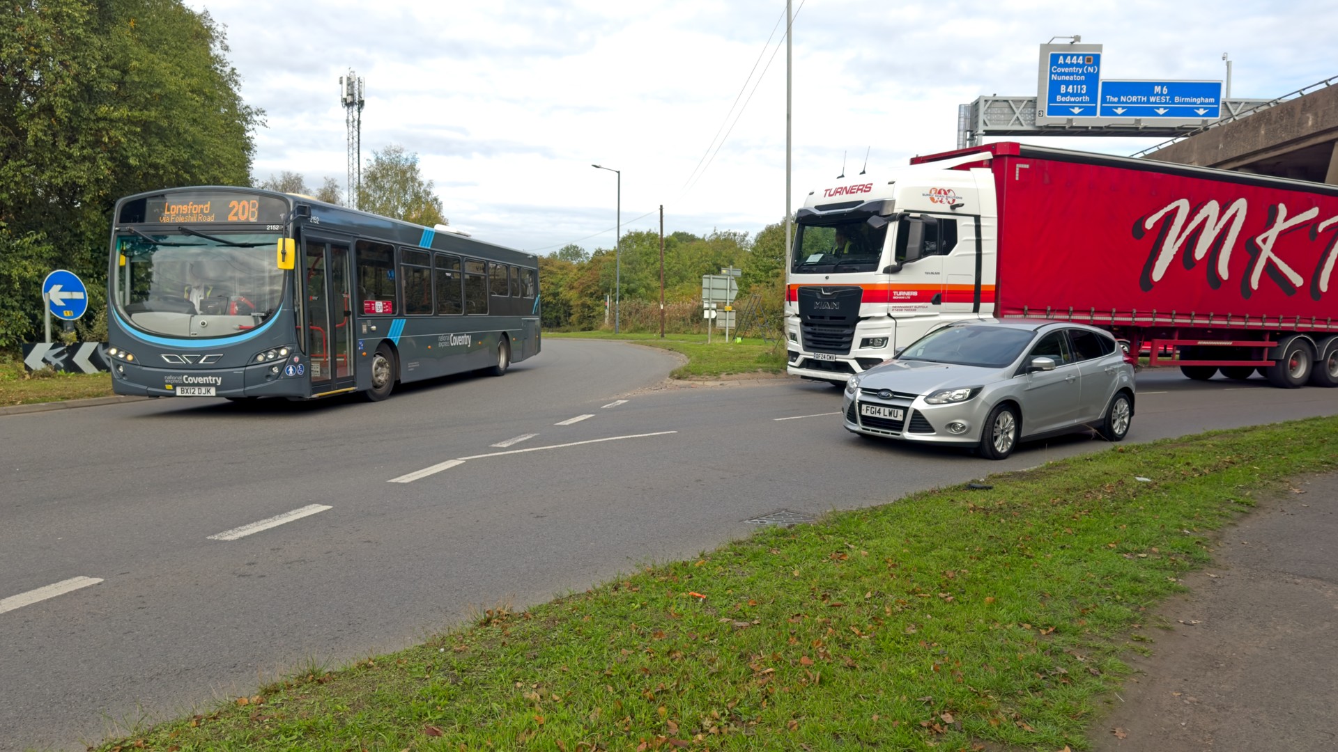 Longford Road meets the roundabout. A car waits to join in the left lane, a lorry waits in the right lane, and a bus passes on the roundabout.