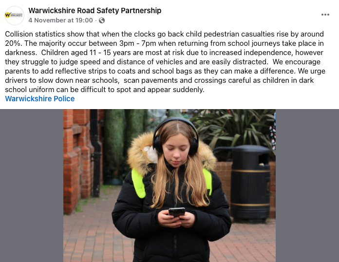 Facebook post from Warwickshire Road Safety Partnership: "Collision statistics show that when the clocks go back child pedestrian casualties rise by around 20%. The majority occur between 3pm - 7pm when returning from school journeys take place in darkness. Children aged 11-15 years are most at risk due to increased independence, however they struggle to judge speed and distance of vehicles and are easily distracted. We encourage parents to add reflective strips to coats and school bags as they can make a difference. We urge drivers to slow down near schools, scan pavements and crossings careful as children in dark school uniform can be difficult to spot and appear suddenly."

Accompanying the post is a photograph of a school child wearing a thick coat with a lowered fur-style lined hood, thick headphones over her ears, eyes down looking at a smartphone screen. She has large high-visibility straps over each shoulder, presumably attached to a backpack. She does not appear to be near a road, where a block paved surface is behind her, a building is just visible to our left, and a waste bin to our right suggesting a courtyard or pedestrianised space of some kind.